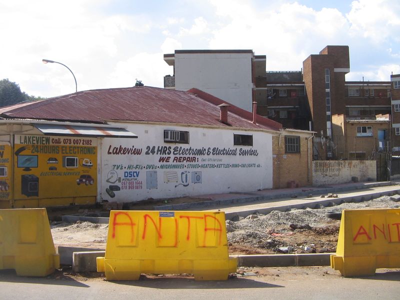 Street-level view of a commercial retail property featuring painted masonry walls, corrugated metal roofing, and prominent signage for electronic repair services.
