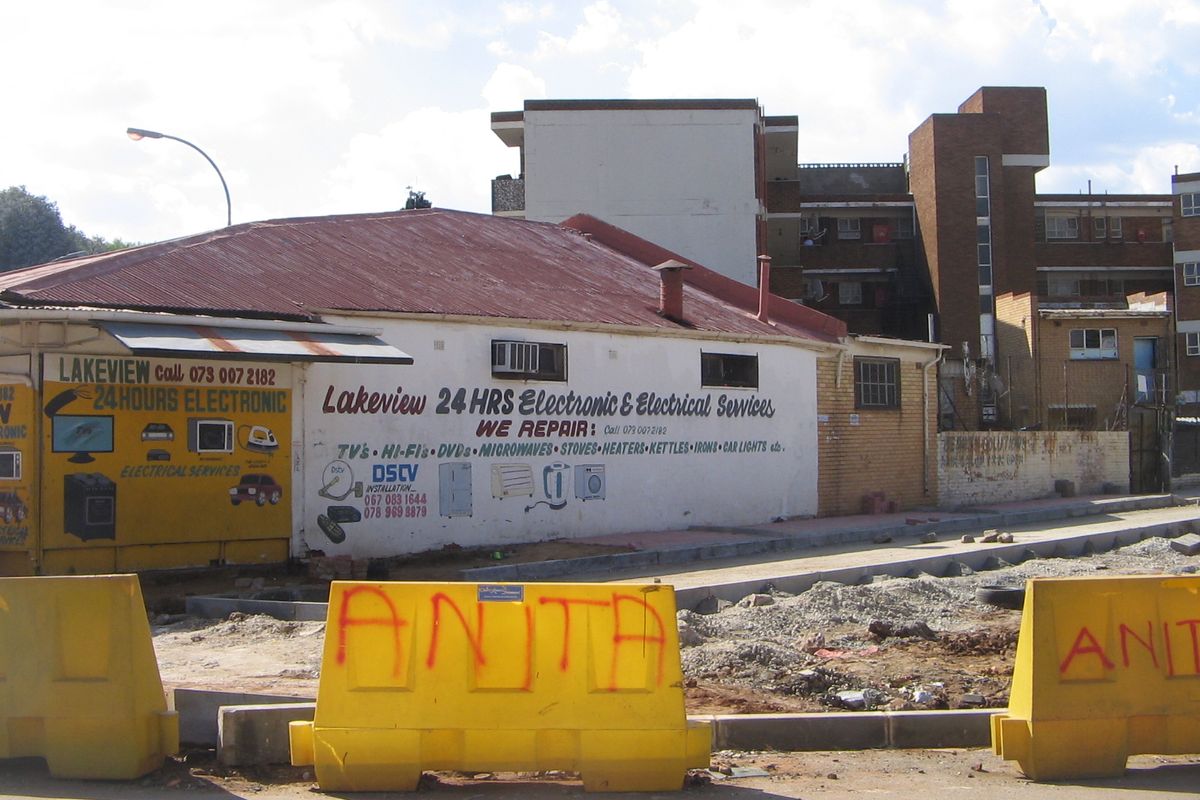 Street-level view of a commercial retail property featuring painted masonry walls, corrugated metal roofing, and prominent signage for electronic repair services.