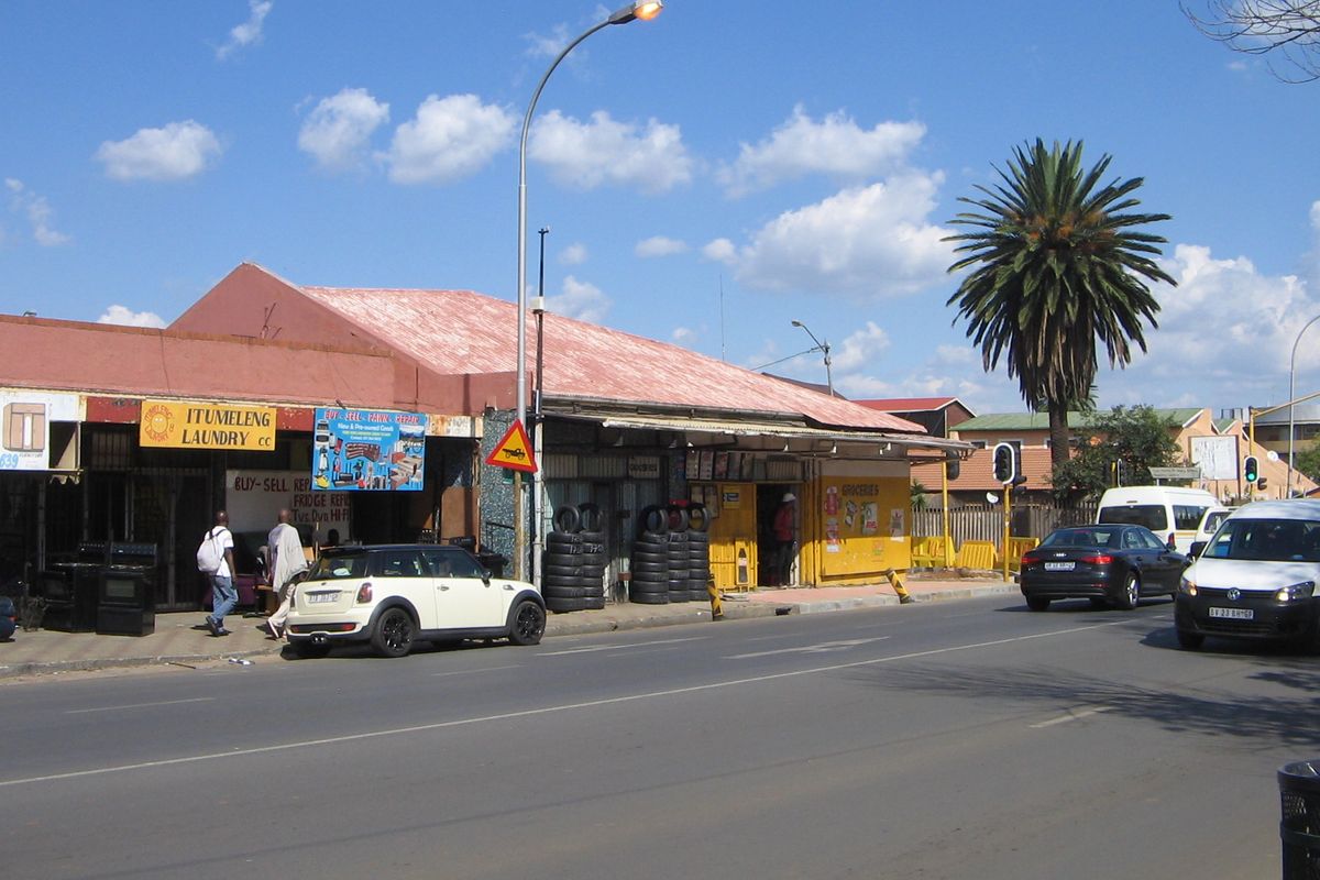Street-level view of a retail property featuring a metal roof and shopfronts along a busy road.