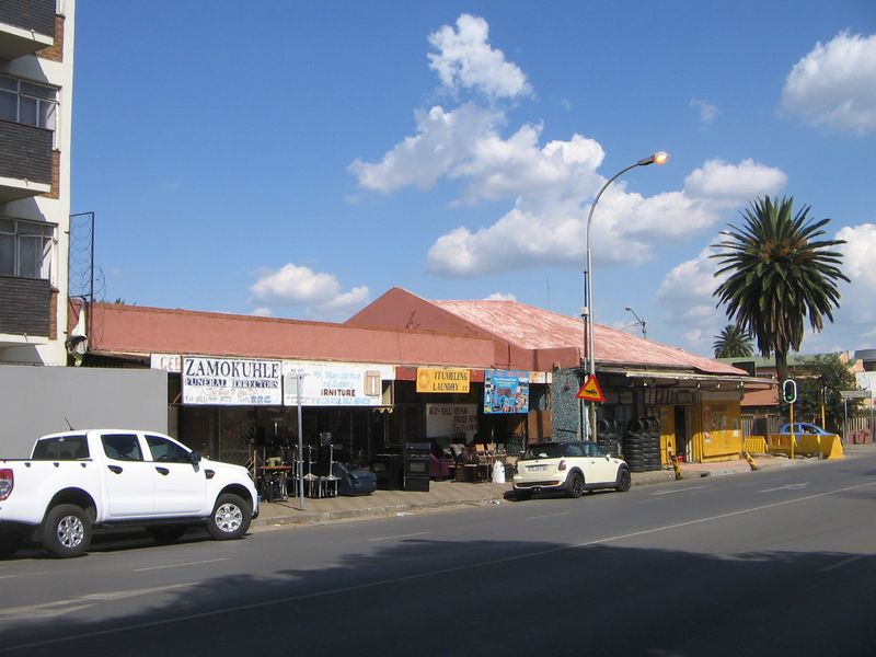 Street-level view of a commercial retail property featuring multiple shopfronts with signage and a metal roof structure.