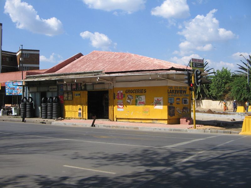 Street-level view of a retail property featuring a corrugated metal roof, security shutters, and prominent street-facing signage on a corner lot.