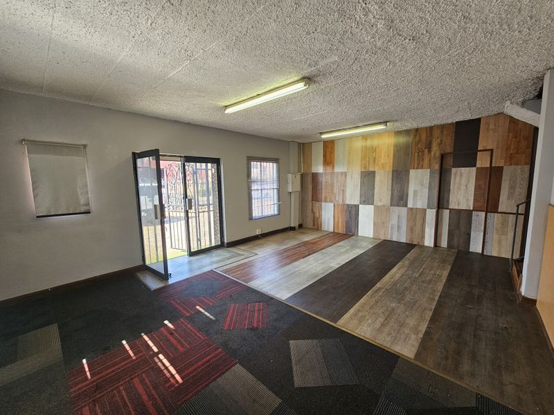 Open-plan retail entry area featuring a mix of carpet and laminate flooring, wood-paneled feature wall, and secure glass entrance door.