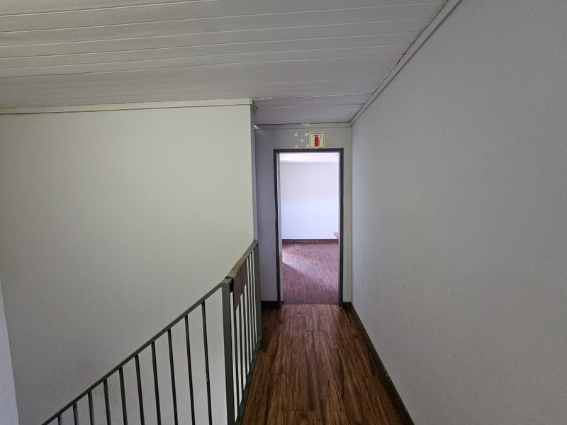 A functional hallway featuring laminate flooring, a metal balustrade, and a tongue and groove ceiling, leading to an adjacent room.