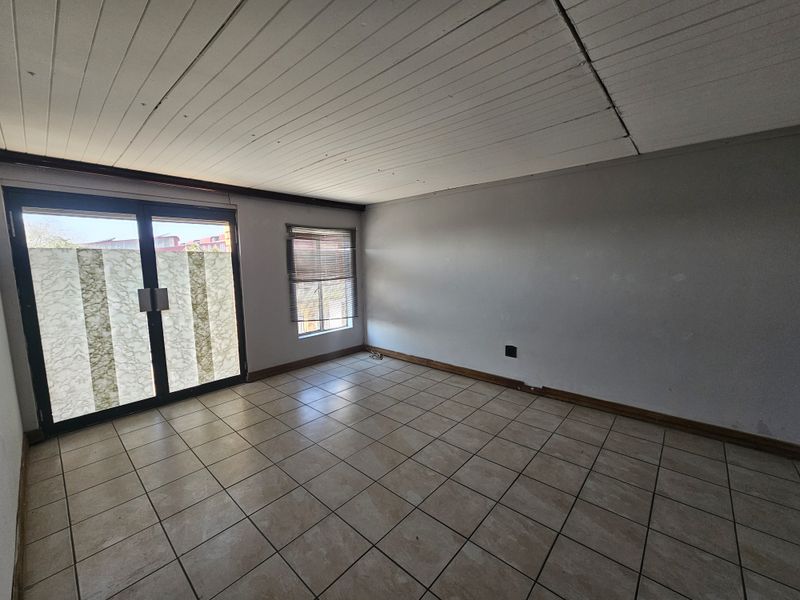 An empty, open-plan living area featuring tiled flooring, timber panel ceiling, and sliding glass doors providing access to the exterior.