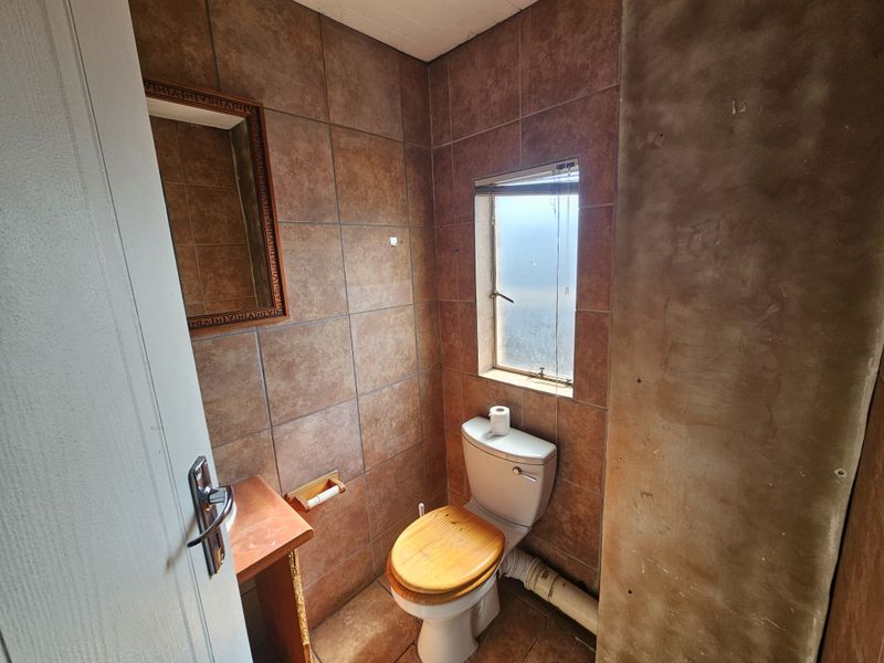 A small bathroom featuring tiled walls and flooring, a standard toilet, and an unfinished wall section requiring cosmetic attention.
