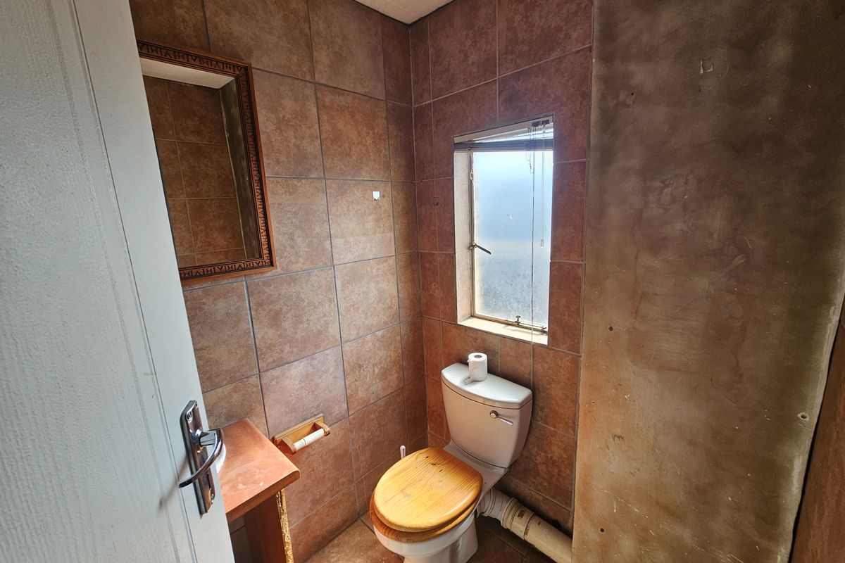 A small bathroom featuring tiled walls and flooring, a standard toilet, and an unfinished wall section requiring cosmetic attention.