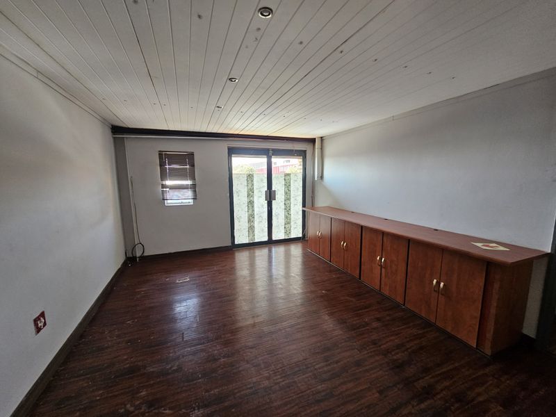 An empty office space featuring laminate flooring, built-in cabinetry, and recessed ceiling lighting with access to an exterior area via glass sliding doors.