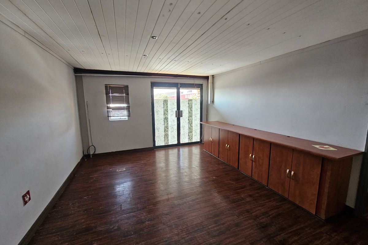An empty office space featuring laminate flooring, built-in cabinetry, and recessed ceiling lighting with access to an exterior area via glass sliding doors.