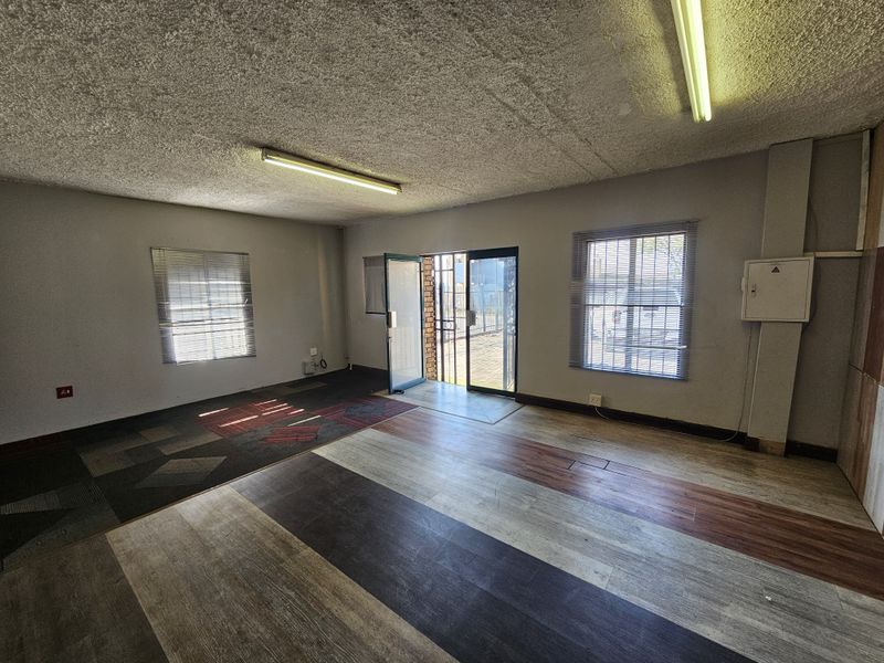 An empty open-plan retail space featuring textured ceilings, fluorescent lighting, and a secure entrance, offering a blank canvas for commercial customization.
