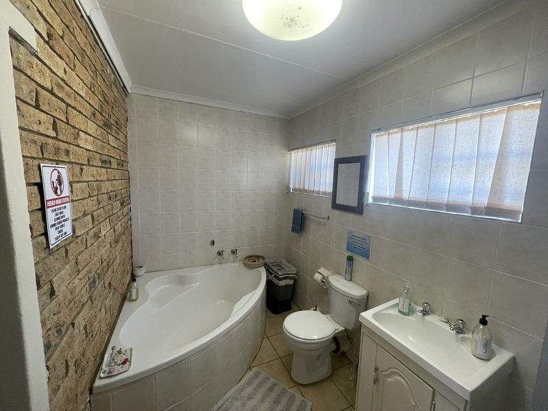 A functional bathroom featuring a corner bathtub, vanity cabinet, and a distinctive exposed brick feature wall with tiled surrounds.