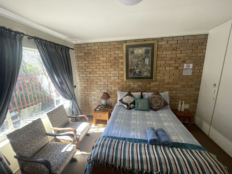 A bedroom featuring an exposed brick feature wall, built-in wardrobe storage, and natural light from a large window.