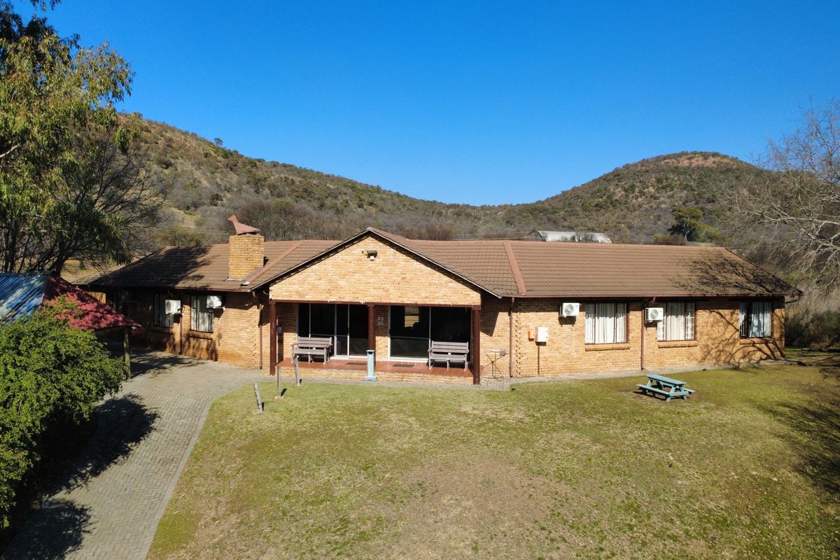 Aerial view of a single-story brick farmhouse featuring a tiled roof, covered patio area, and paved driveway set against a scenic hilly landscape.
