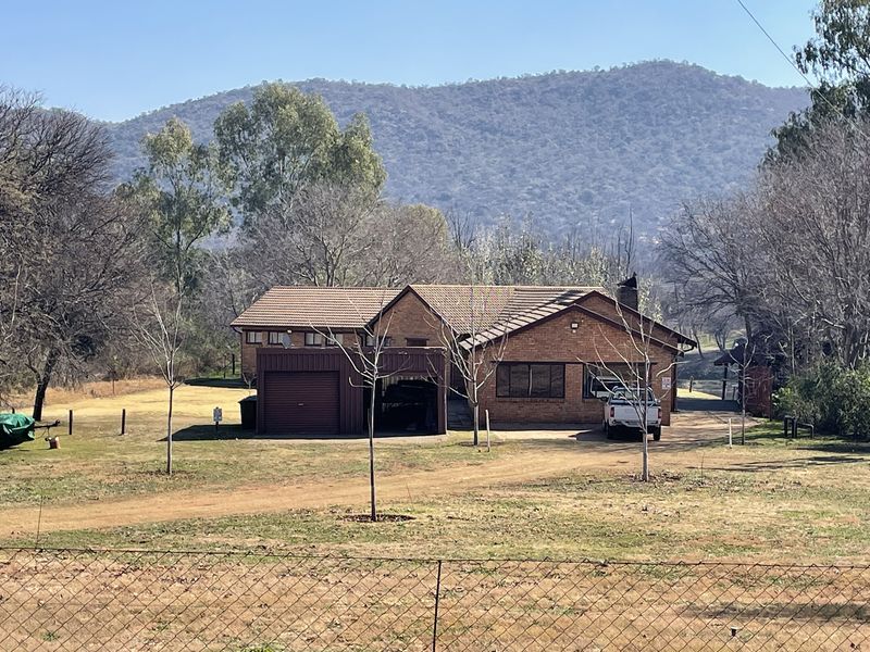 A brick-faced farm residence featuring a tiled roof, attached garage, and driveway, set against a scenic mountain backdrop.