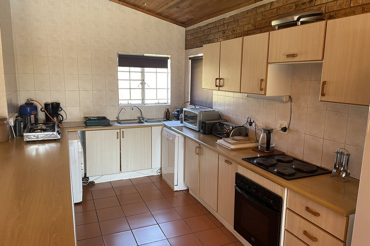 Functional kitchen featuring built-in cabinetry, laminate countertops, electric hob, oven, and double sink, finished with tiled splashbacks and a timber ceiling.