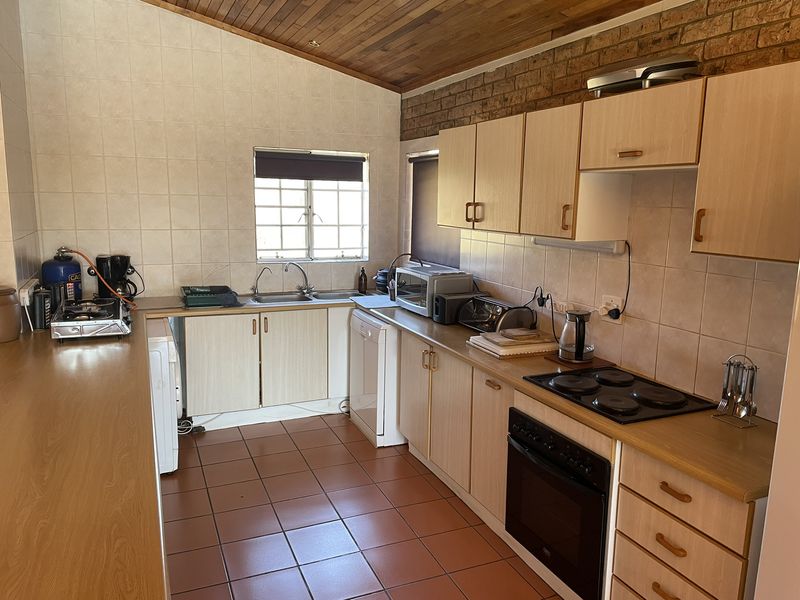 Functional kitchen featuring built-in cabinetry, laminate countertops, electric hob, oven, and double sink, finished with tiled splashbacks and a timber ceiling.