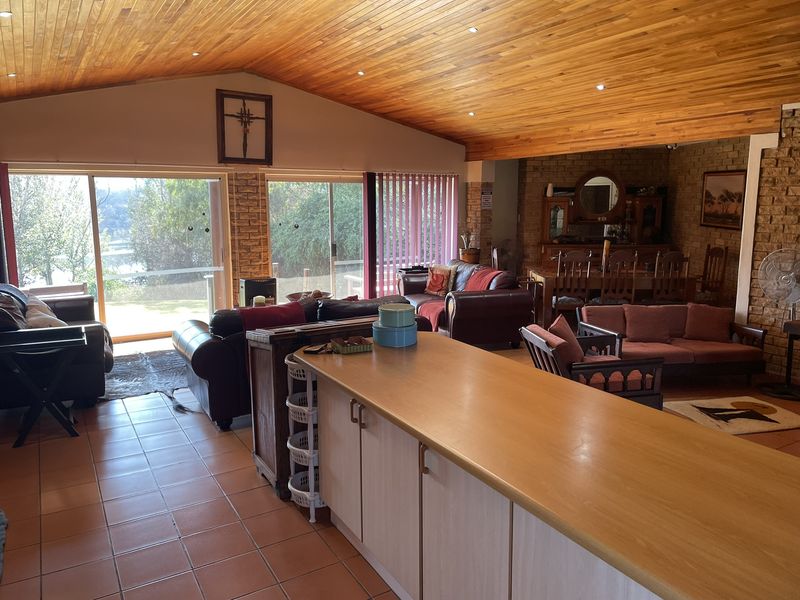 Spacious open-plan living and dining area featuring a vaulted timber ceiling, exposed brick walls, tiled flooring, and large sliding doors leading to the exterior.