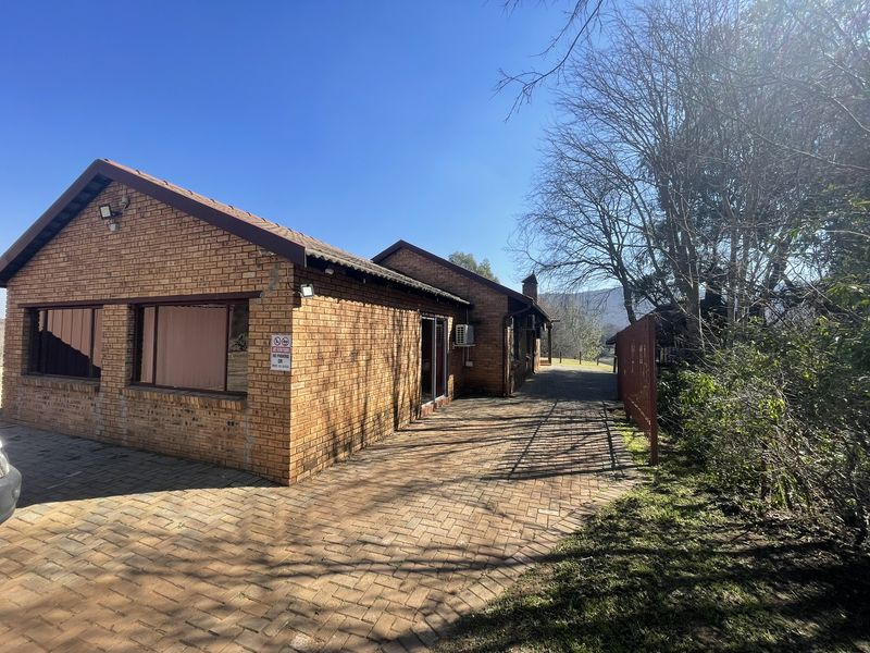A well-maintained face brick farm building featuring a paved driveway, tiled roof, and exterior security lighting under a clear blue sky.