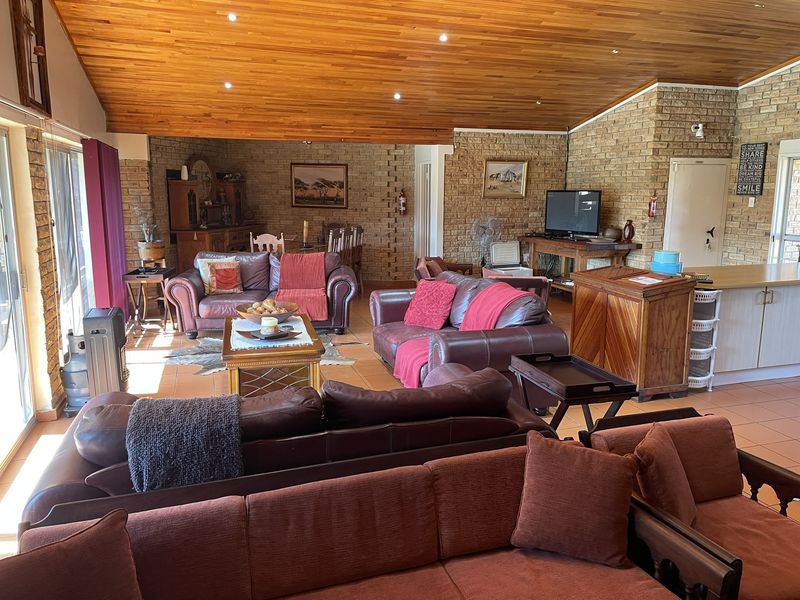 Spacious open-plan living area featuring a warm timber-clad ceiling, facebrick walls, and tiled flooring, creating a comfortable and inviting farmhouse-style interior.