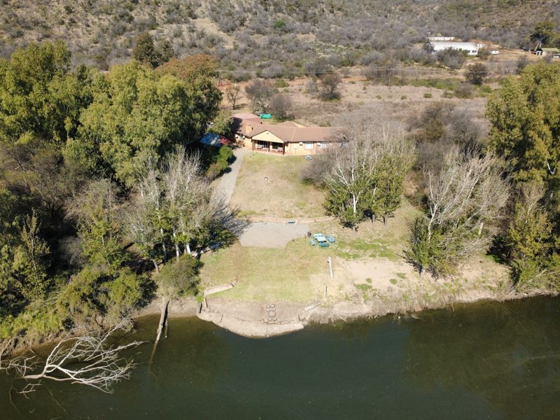 Aerial view of a farm property featuring a main dwelling, expansive grounds, mature trees, and direct river frontage.
