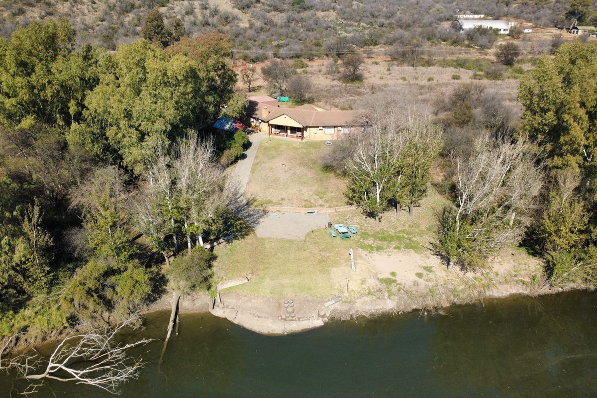 Aerial view of a farm property featuring a main dwelling, expansive grounds, mature trees, and direct river frontage.