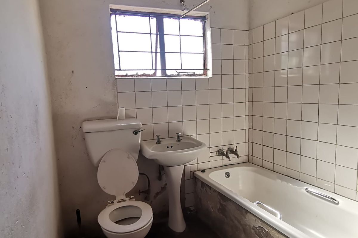 A dated bathroom featuring a pedestal basin, toilet, and bathtub with tiled splashbacks, requiring significant renovation and cosmetic repairs to the walls and finishes.