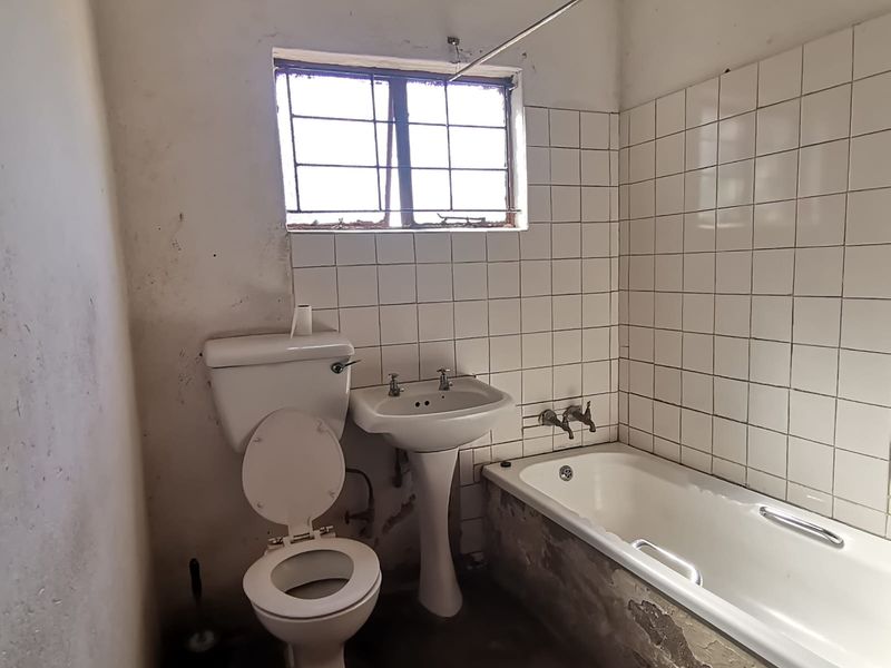 A dated bathroom featuring a pedestal basin, toilet, and bathtub with tiled splashbacks, requiring significant renovation and cosmetic repairs to the walls and finishes.