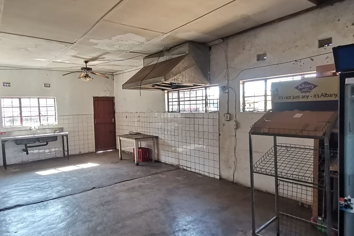 A spacious, industrial-style kitchen area featuring a stainless steel sink, extractor fan, and tiled splashbacks, requiring significant renovation and repair.
