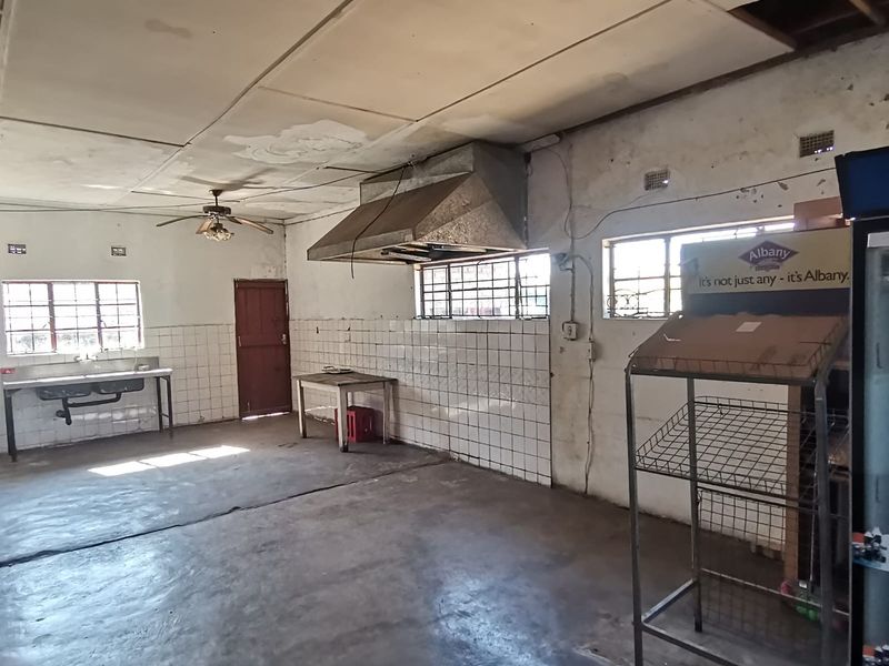 A spacious, industrial-style kitchen area featuring a stainless steel sink, extractor fan, and tiled splashbacks, requiring significant renovation and repair.