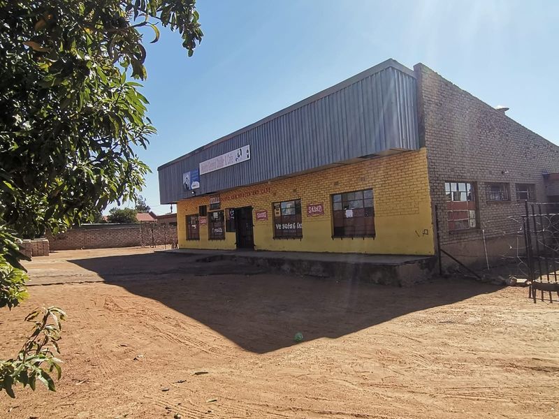 Front view of a commercial building featuring brick construction, metal roof cladding, and a large unpaved yard area.