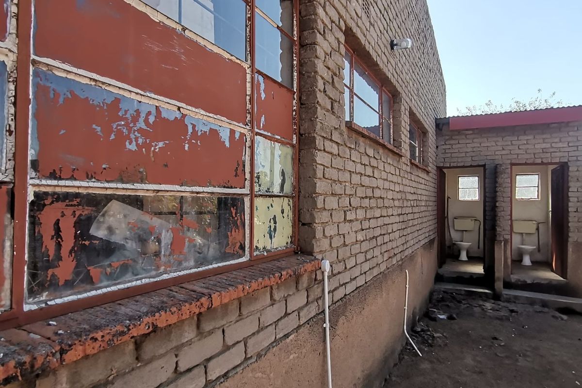 Rear exterior view of a brick building featuring weathered steel-framed windows and two external toilet cubicles with basic sanitary fixtures.