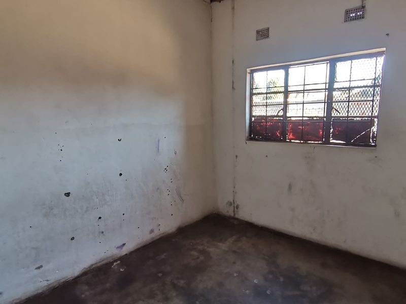 An empty, dated bedroom featuring security bars on the window and requiring significant cosmetic refurbishment to the walls, ceiling, and flooring.