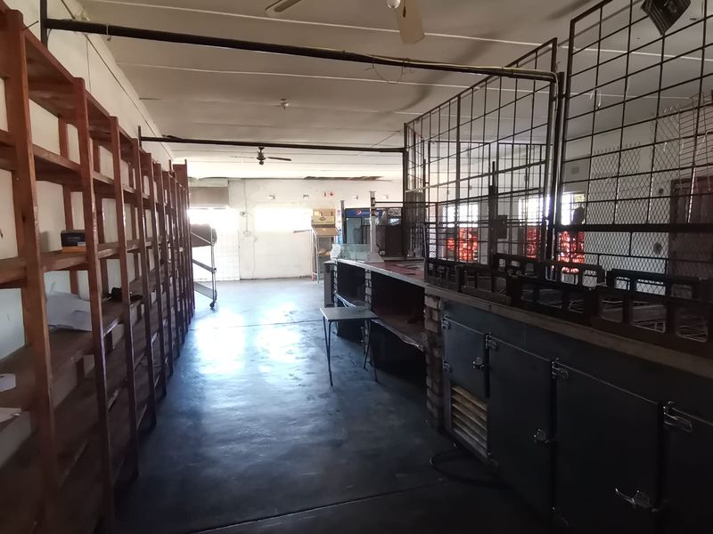 A vacant utility or storage space featuring concrete floors, built-in shelving units, and metal security partitioning, suitable for commercial or industrial use.