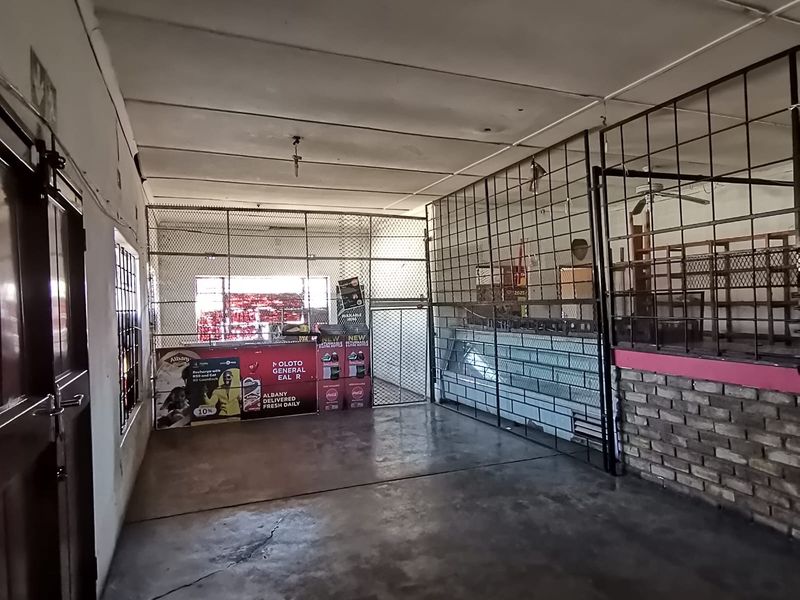 A utilitarian commercial space featuring concrete flooring, security mesh partitioning, and exposed brickwork, suitable for storage or retail operations.