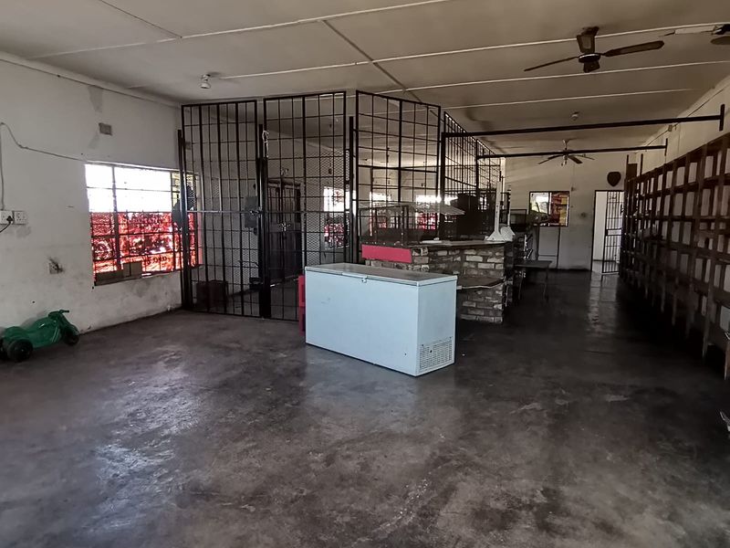 Spacious open-plan commercial area featuring concrete flooring, ceiling fans, and built-in security grilles, suitable for retail or workshop use.