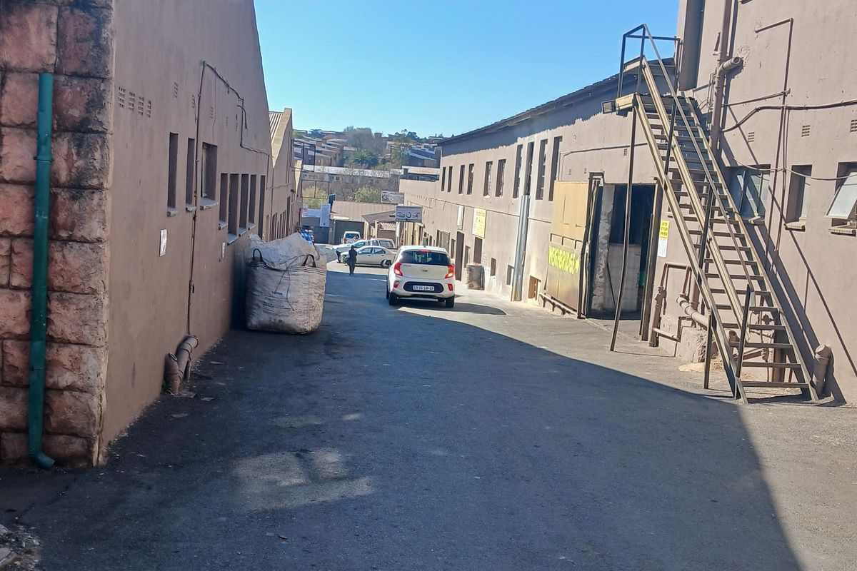 Rear industrial access area featuring asphalt paving, masonry building facades, and an external metal staircase for upper-level access.