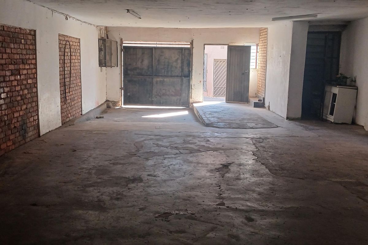 Spacious industrial garage or workshop area featuring concrete flooring, exposed brick accents, and secure metal access doors, suitable for storage or light industrial use.