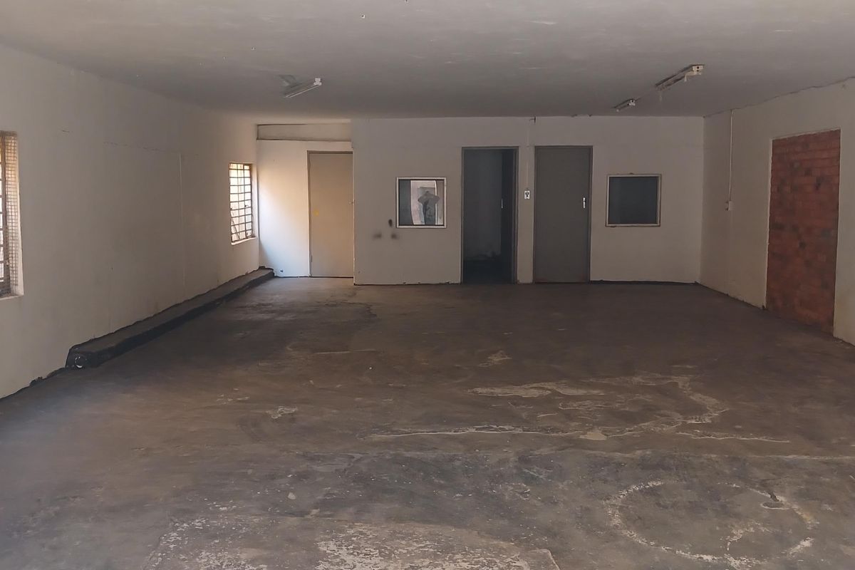 Spacious industrial utility area featuring concrete flooring, exposed brick accents, and security-barred windows, offering a versatile blank canvas for various commercial or storage uses.