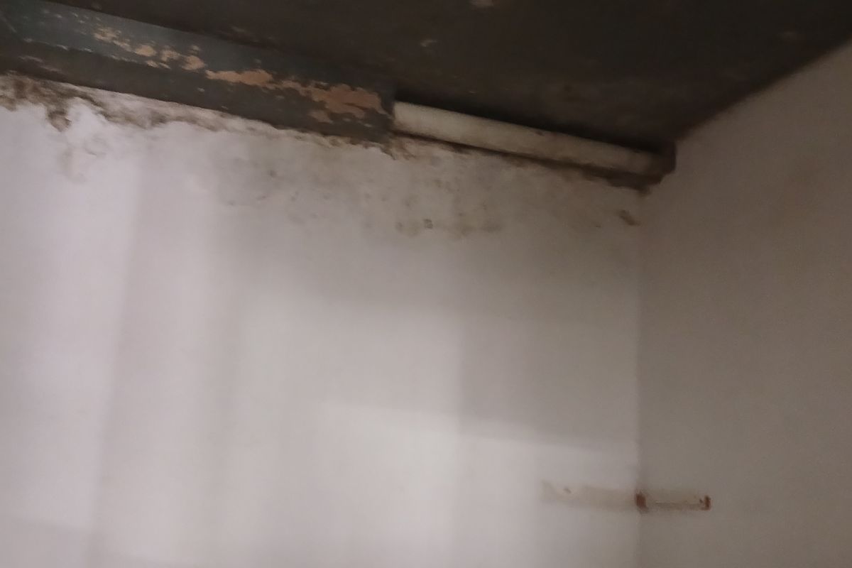 An empty utility space showing significant wall surface deterioration and moisture damage, requiring maintenance and repair.
