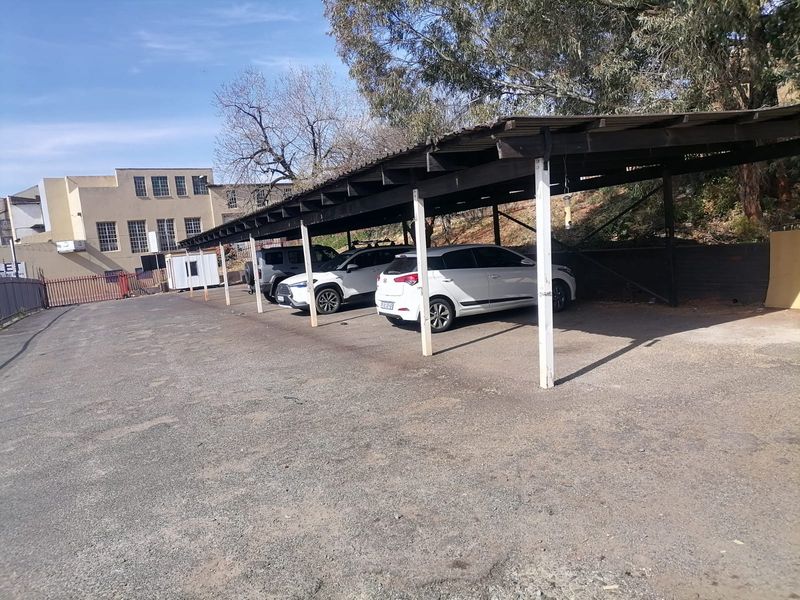 Industrial property exterior featuring a covered parking area with asphalt driveway and perimeter fencing.