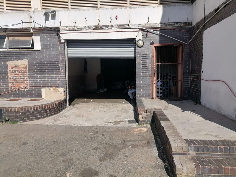 Industrial garage entrance featuring a roller shutter door, security gate, and concrete ramp access with visible wear to the surrounding brick facade.