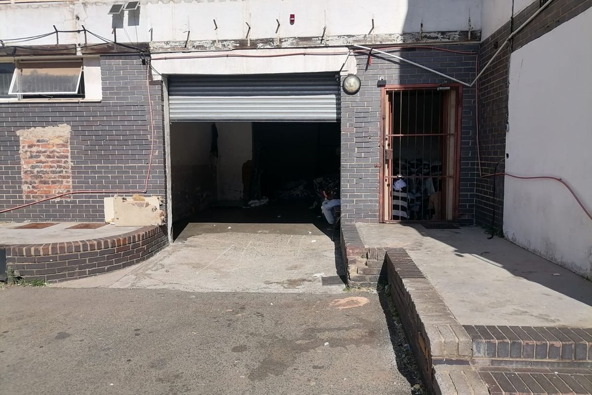 Industrial garage entrance featuring a roller shutter door, security gate, and concrete ramp access with visible wear to the surrounding brick facade.