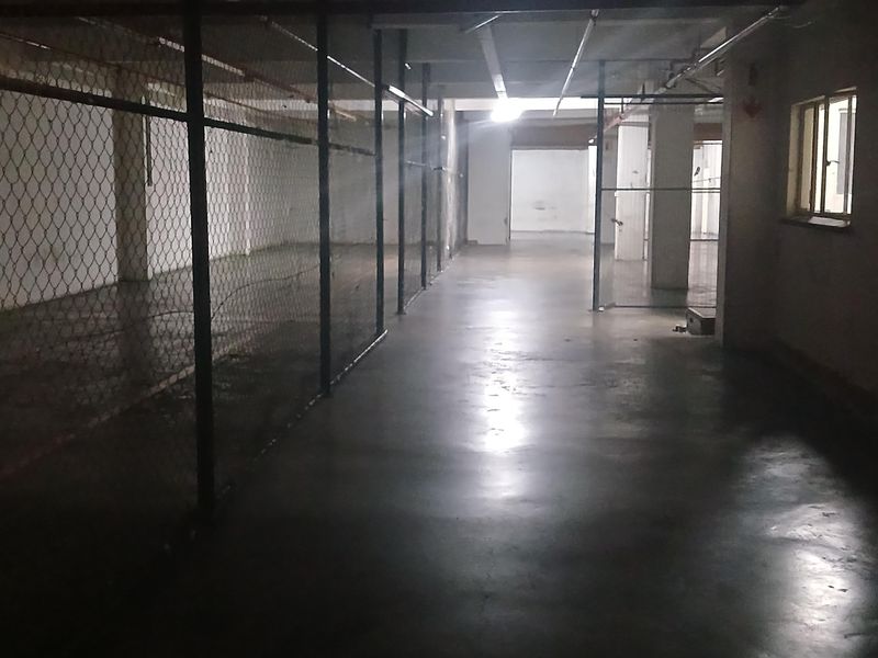 An industrial utility space featuring concrete flooring, chain-link partitions, and exposed ceiling infrastructure, suitable for storage or workshop use.