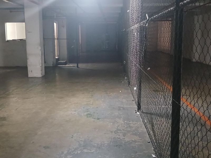 An expansive, open-plan industrial utility space featuring concrete flooring, structural columns, and secure chain-link partitioning, suitable for storage or workshop use.
