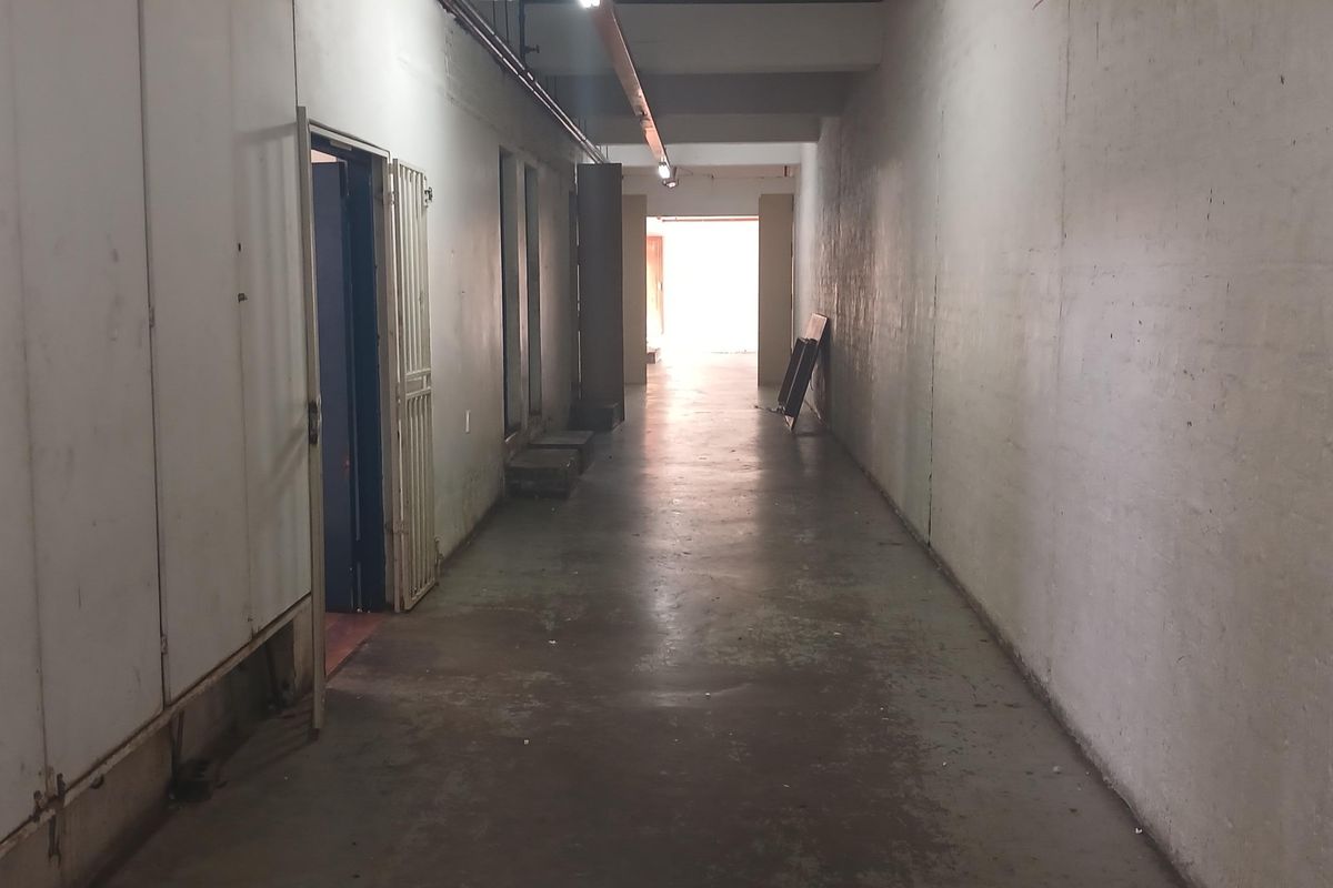 A long industrial hallway featuring concrete flooring, exposed conduit lighting, and security gate access, presenting a functional and utilitarian space.