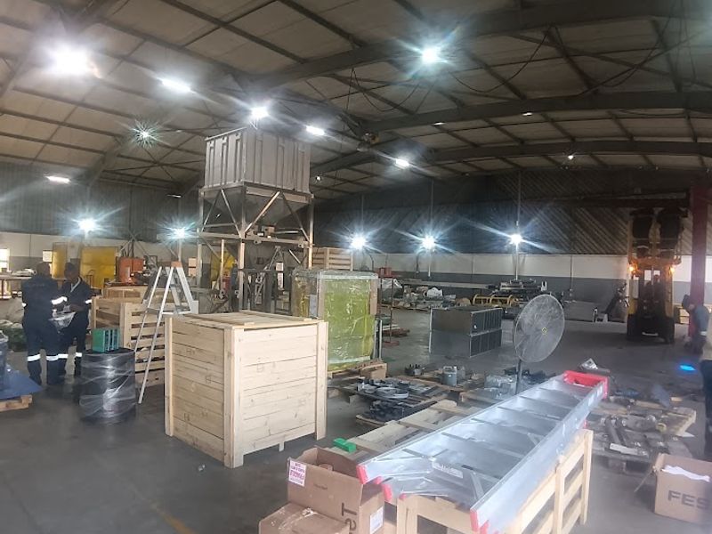 Spacious industrial warehouse facility featuring high-bay lighting, concrete flooring, and an integrated industrial hopper system, suitable for manufacturing or storage operations.