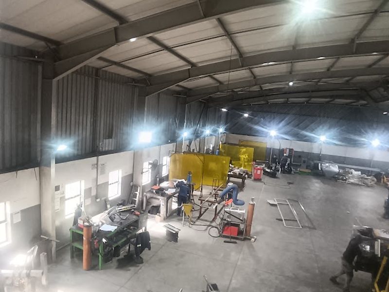 Spacious industrial workshop featuring high ceilings with exposed steel trusses, concrete flooring, and functional high-bay lighting throughout the workspace.