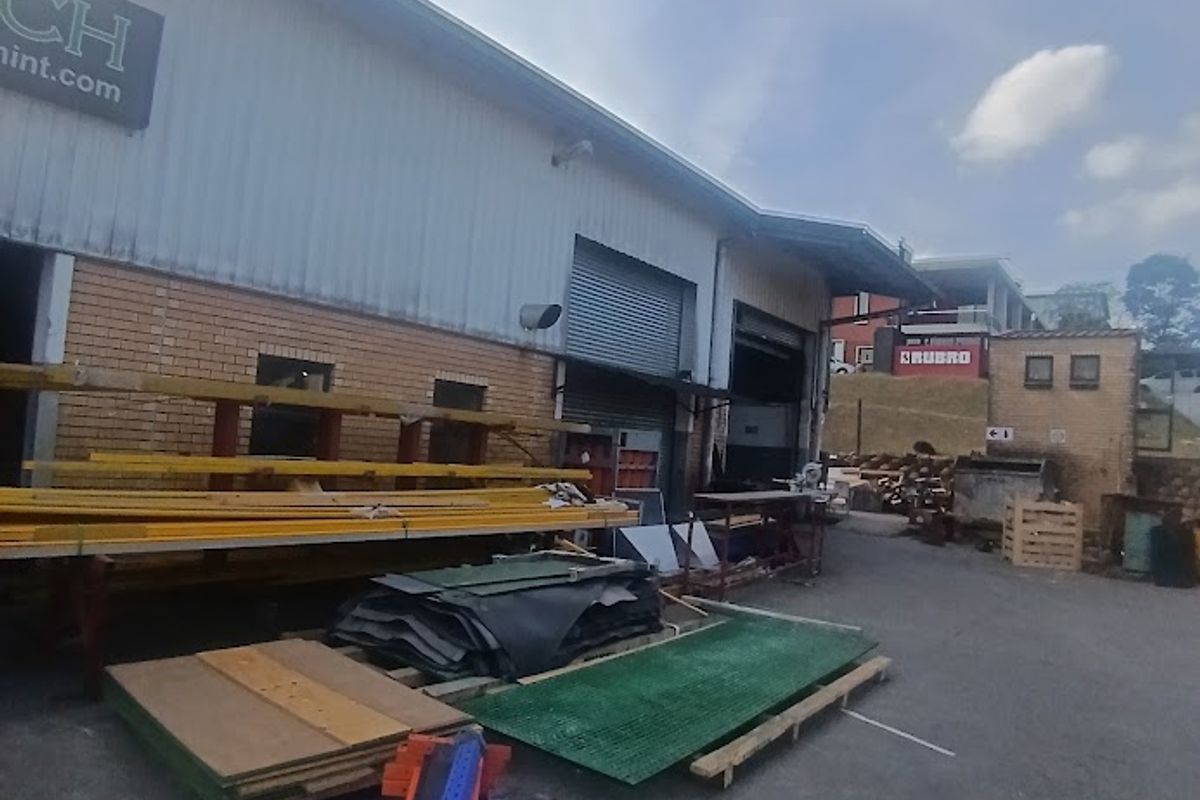 Rear industrial yard area featuring a roller shutter door, metal cladding, and brick facade, providing functional access for loading and storage.