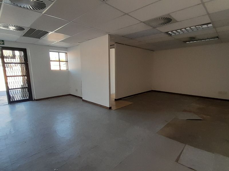 An empty office space featuring a suspended ceiling, recessed lighting, and a security gate at the entrance, requiring flooring repairs.