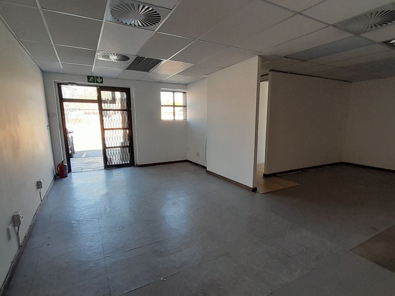 An empty office space featuring a suspended ceiling, recessed lighting, and a security gate, providing a blank canvas for professional customization.