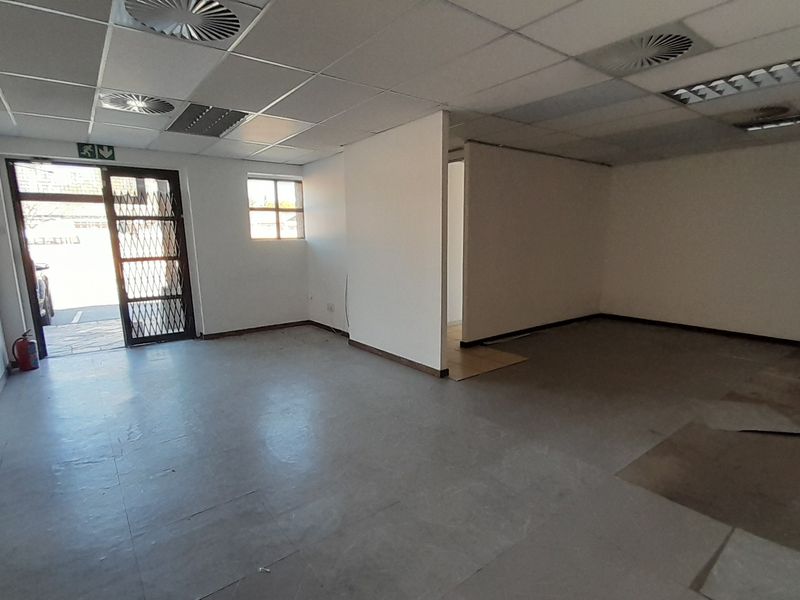 An empty office space featuring a suspended ceiling, recessed lighting, and a security gate at the entrance, requiring minor flooring repairs.
